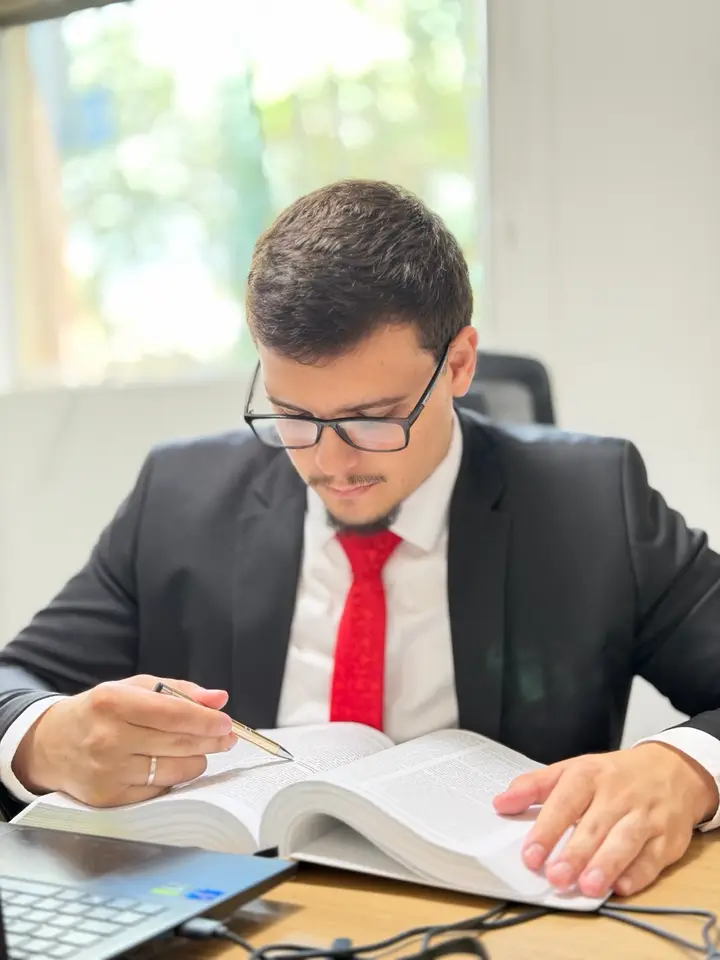 Pedro Crepaldi lendo um livro de direito, caneta na mão, em uma mesa com notebook